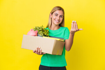 Young Uruguayan girl making a move while picking up a box full of things isolated on yellow...