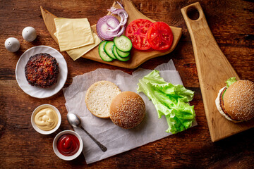 Ingredients for a classic hamburger. Grilled meat, vegetables, greens, sauces near a sesame bun. Wooden background. Cooking hamburger or cheeseburger.
