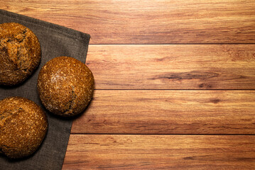 Homemade wholemeal loaves on a gray dishcloth. Light wooden table background, top view and space for text.