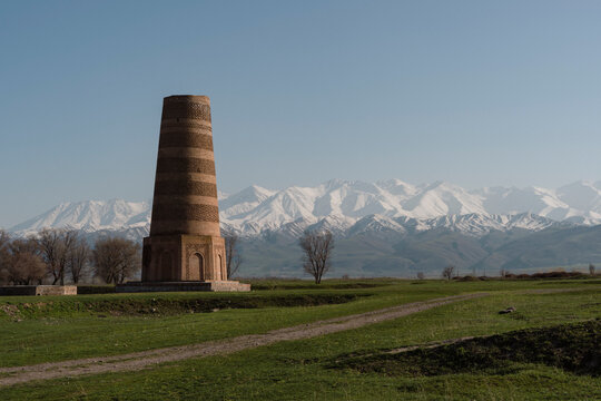 Burana tower which is an old and large minaret in the ruins of the ancient site of Balasagun with tombstones known as balbas in the foreground, Kyrgyzstan.