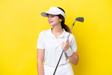 young caucasian woman playing golf isolated on yellow background looking side