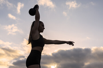 Strong sportswoman lifting kettlebell at sunrise