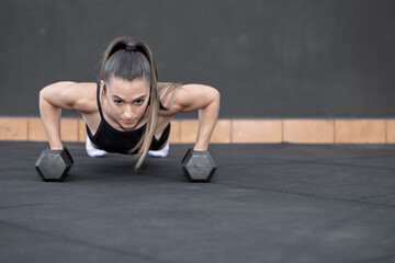 Fototapeta na wymiar Sportswoman doing push ups on dumbbells