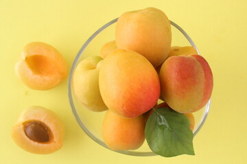 A transparent bowl full of apricot with green leaf isolated on yellow background. Cut fruit with detail. Sitting view and close up shooting.