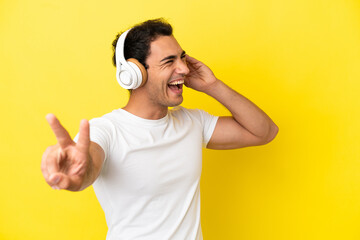 Caucasian handsome man over isolated yellow background listening music and singing