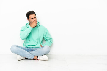 Caucasian handsome man sitting on the floor having doubts and with confuse face expression