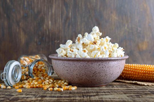 A large bowl of popcorn, corn grains and corncob on a wooden table. Close-up.