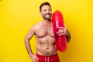 Middle age caucasian man holding inflatable donut isolated on yellow background posing with arms at...