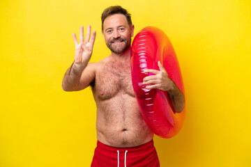 Middle age caucasian man holding inflatable donut isolated on yellow background happy and counting four with fingers
