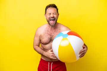 Middle age caucasian man holding beach ball isolated on yellow background smiling a lot