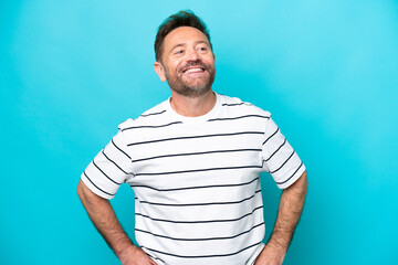 Middle age caucasian man isolated on blue background posing with arms at hip and smiling