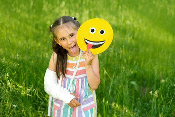 Funny girl with a fractured arm and cast shows tongue, holding amusing humorous smile face in...