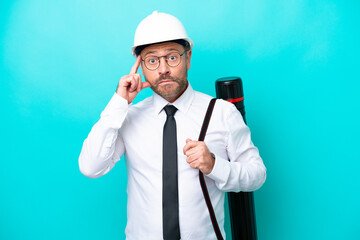 Middle age architect man with helmet and holding blueprints isolated on blue background thinking an idea