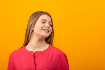 Fototapeta premium Close up portrait of young girl smiling sweetly and looking away. Teenage girl in red shirt on an orange background.