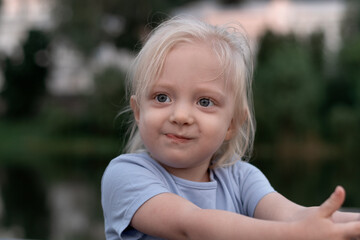 Portrait of little blonde girl with big eyes wears blue T-shirt and looks into the distance. Childlike spontaneity.