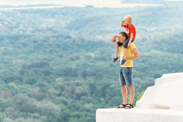 Dad and son are standing on observation deck holding hand above eyes and peering into distance. Boy sits on the mans shoulders.