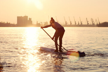 Silhouette of boy on stand up paddle board (SUP) rowing at dawn on Danube river at cold season