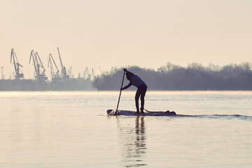 Teenager rowing on stand up paddle board at dawn on Danube river at cold season