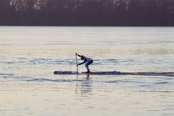 Fototapeta na wymiar Teenager boy rowing on SUP (stand up paddle board) at Danube river at cold season