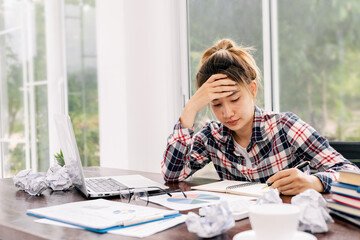 Woman stressed about work at home office and look at something on the laptop screen, The stress gave her a huge headache.