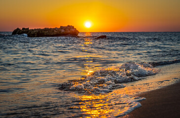 Warm waves of the Mediterranean sea and a sandy beach at sunrise