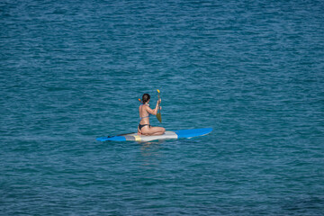 A girl with an oar floats on a board on the sea