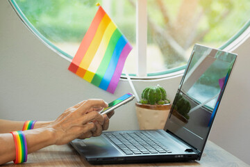 senior woman hands wear rainbow lgbt wristband is using smartphone,lgbt flag and laptop on...