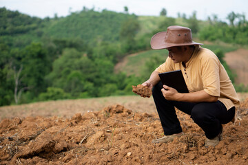 Asian agronomist is checking quality of soil in agriculture land before growing plants, holds smart tablet. Concept : research and analyze soil and environment, use wireless technology internet.