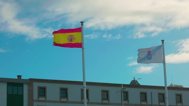 The flag of Spain and Galicia develops in the wind, blue sky with clouds.