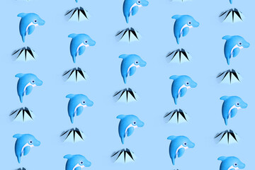 Toy dolphin jumps out of a torn hole in blue paper. Dolphin pattern.