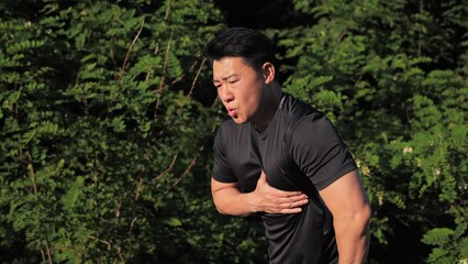 Asian Athlete running on the track feels a sudden chest pain and stops. Heart failure. Health problems. Takihardia. Sportsmen holds his hand behind his chest, difficulty breathing, be out of breath.