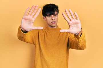 Handsome hipster young man wearing casual yellow sweater doing frame using hands palms and fingers, camera perspective