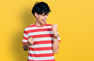 Handsome hipster young man wearing casual striped t shirt very happy and excited doing winner gesture with arms raised, smiling and screaming for success. celebration concept.