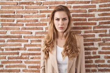 Beautiful blonde woman standing over bricks wall skeptic and nervous, frowning upset because of problem. negative person.