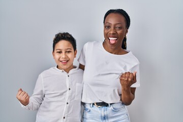 Young mother and son standing together over white background very happy and excited doing winner gesture with arms raised, smiling and screaming for success. celebration concept.