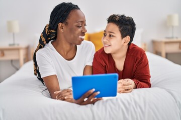 Obraz premium African american mother and son using touchpad lying on bed at bedroom