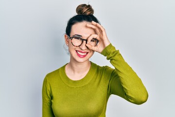 Young hispanic girl wearing casual clothes and glasses doing ok gesture with hand smiling, eye looking through fingers with happy face.