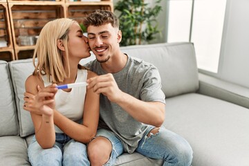 Young caucasian couple smiling happy holding pregnacy test at home.