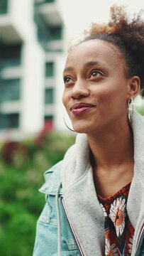 VERTICAL VIDEO: Closeup, nice African girl with ponytail wearing denim jacket, in crop top with national pattern, drinks morning coffee against the backdrop of modern buildings. Slow motion