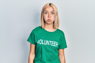 Beautiful blonde woman wearing volunteer t shirt puffing cheeks with funny face. mouth inflated...