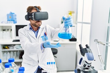 Middle age hispanic man wearing scientist uniform using vr glasses holding test tube at laboratory
