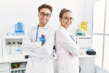 Man and woman wearing scientist uniform standing with arms crossed gesture at laboratory