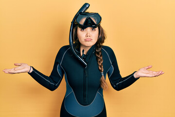 Young hispanic girl wearing diver neoprene uniform clueless and confused with open arms, no idea...
