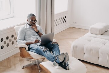 Confident professional at work in front of laptop. Relaxed african businessman in cosy chair.