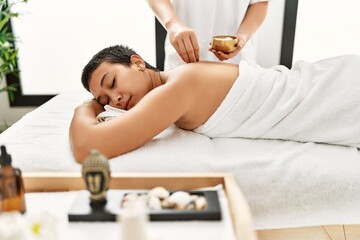 Obraz na płótnie Canvas Young hispanic woman having back massage using salt at beauty center