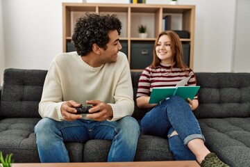 Obraz premium Man playing video game while girlfriend reading book at home.