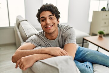 Young hispanic man smiling happy sitting on the sofa at home.