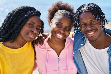 African american friends hugging each other sitting on bench together at seaside
