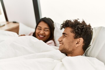 Obraz premium Young latin couple covering with bedsheet lying on the bed at bedroom.