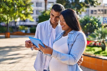 Young latin couple expecting baby using touchpad at park